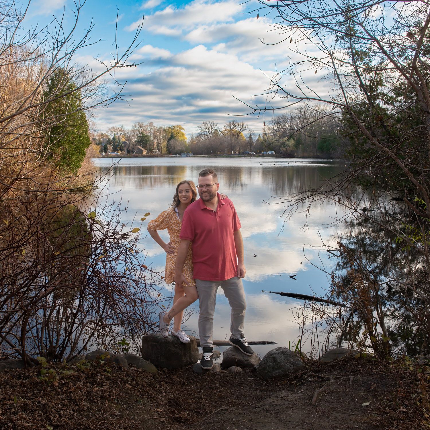 A couple standing on the rocky shore of a lake under a wide cloudy sky