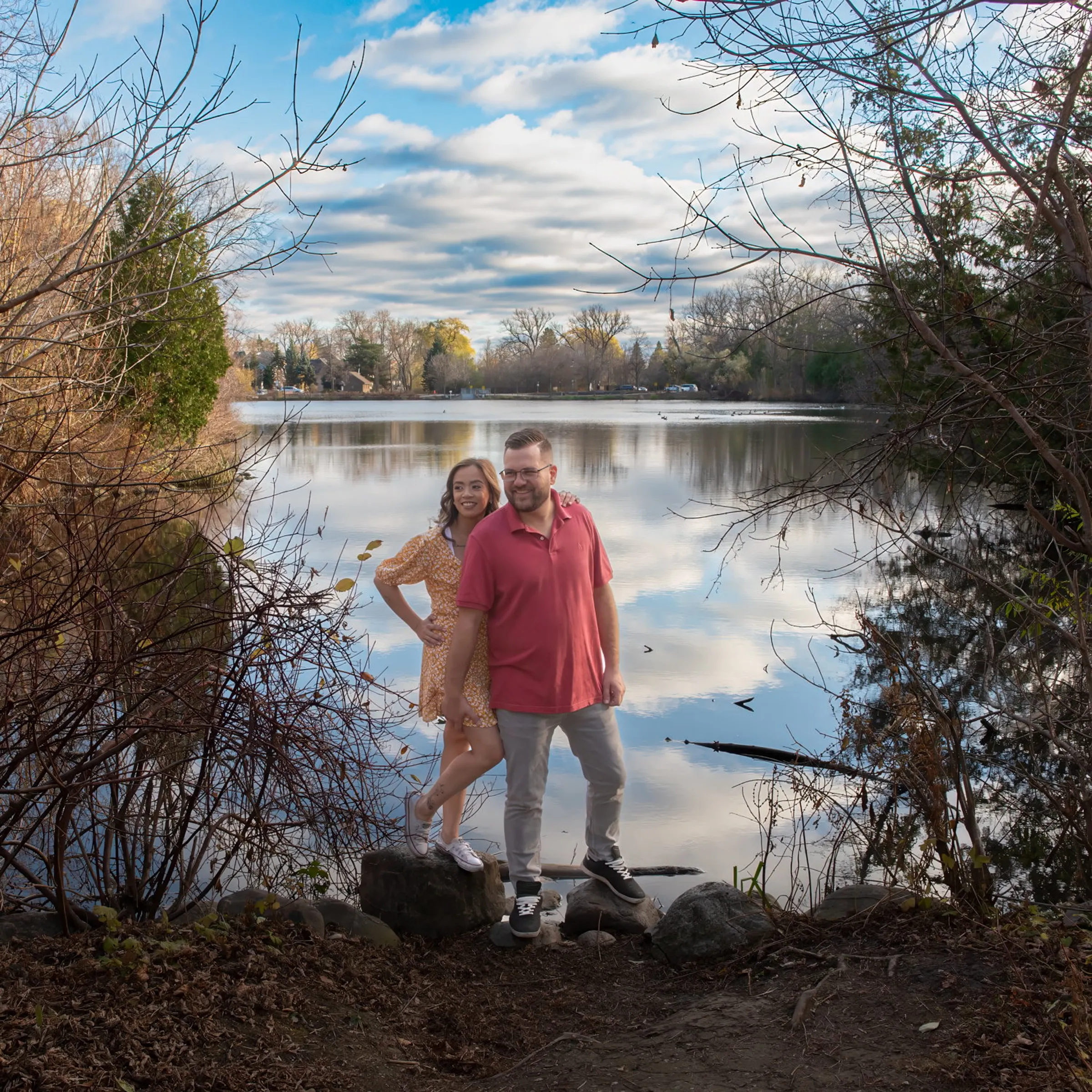 A couple standing on the rocky shore of a lake under a wide cloudy sky