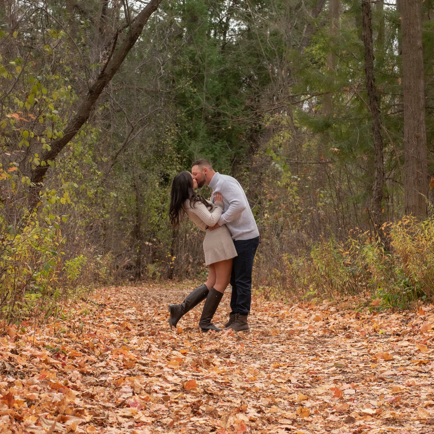 Larissa & Gianluca holding each other in deep autumn leaves at the treeline