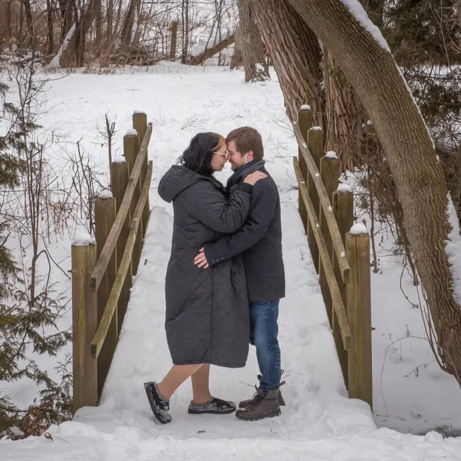 A couple kissing on a snow-covered wooden bridge