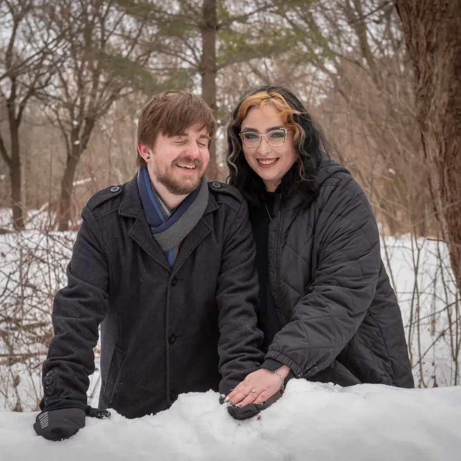 A couple resting on a bank of snow in a bare winter forest