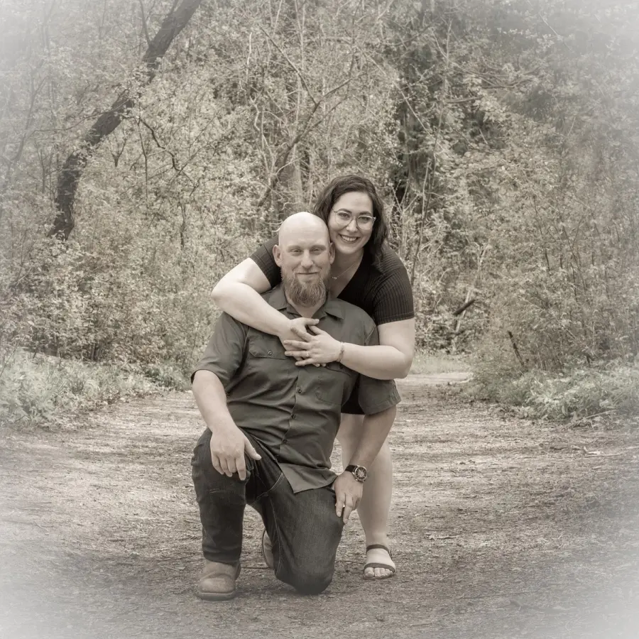 Black-and-white photo of a man kneeling on a park path while his partner leans over his shoulder