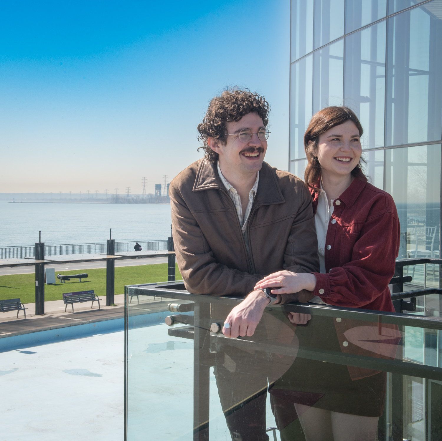 Sydney & Liam at a glass balcony rail with the lake behind them