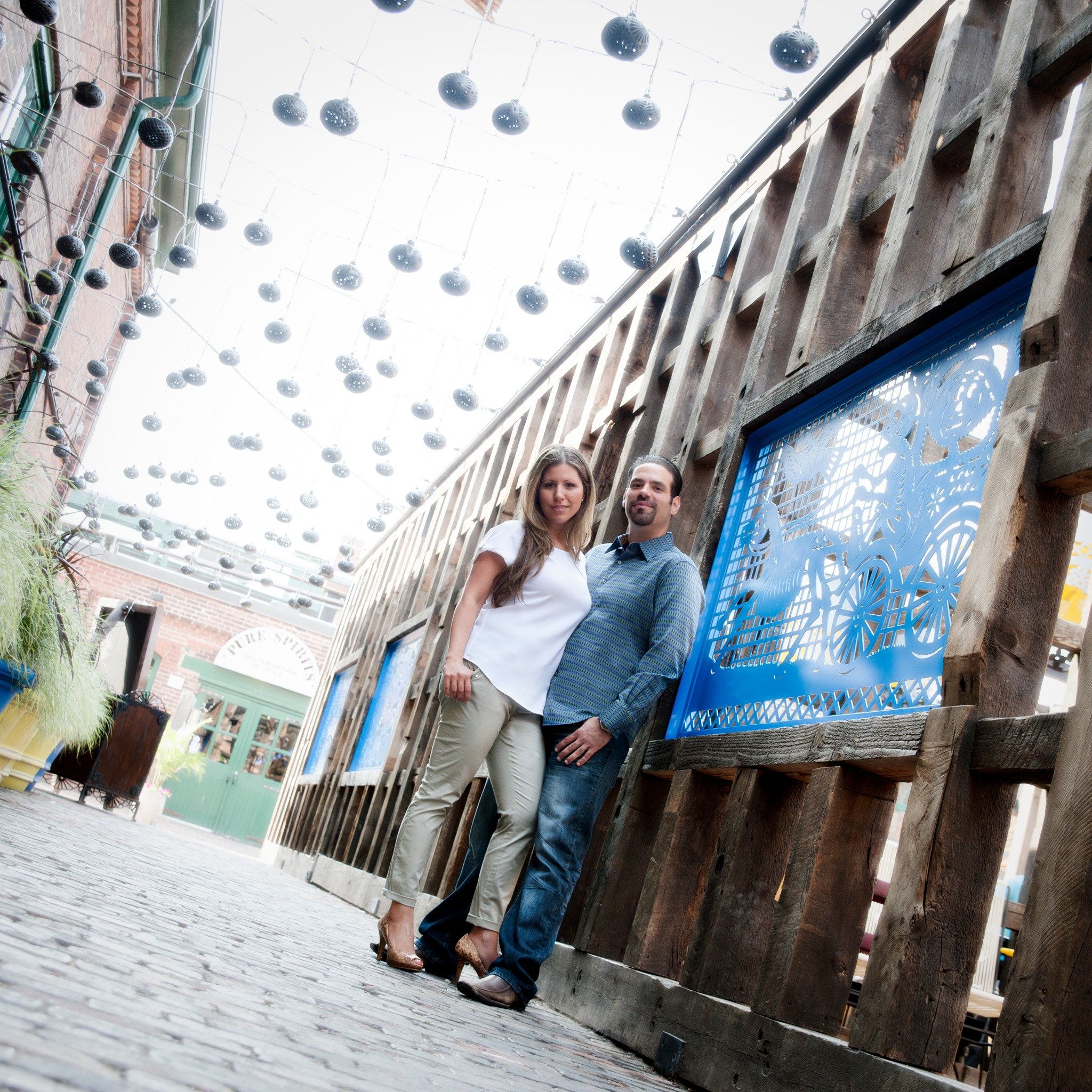 A couple leaning against a weathered wood wall under hanging lanterns in the Distillery District