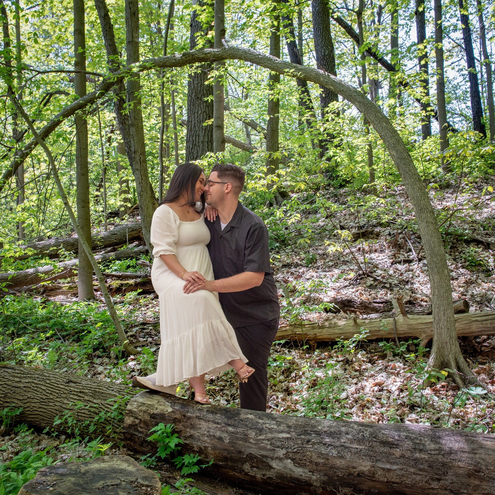 A couple about to kiss under an arching bare branch in a leafy spring woodland