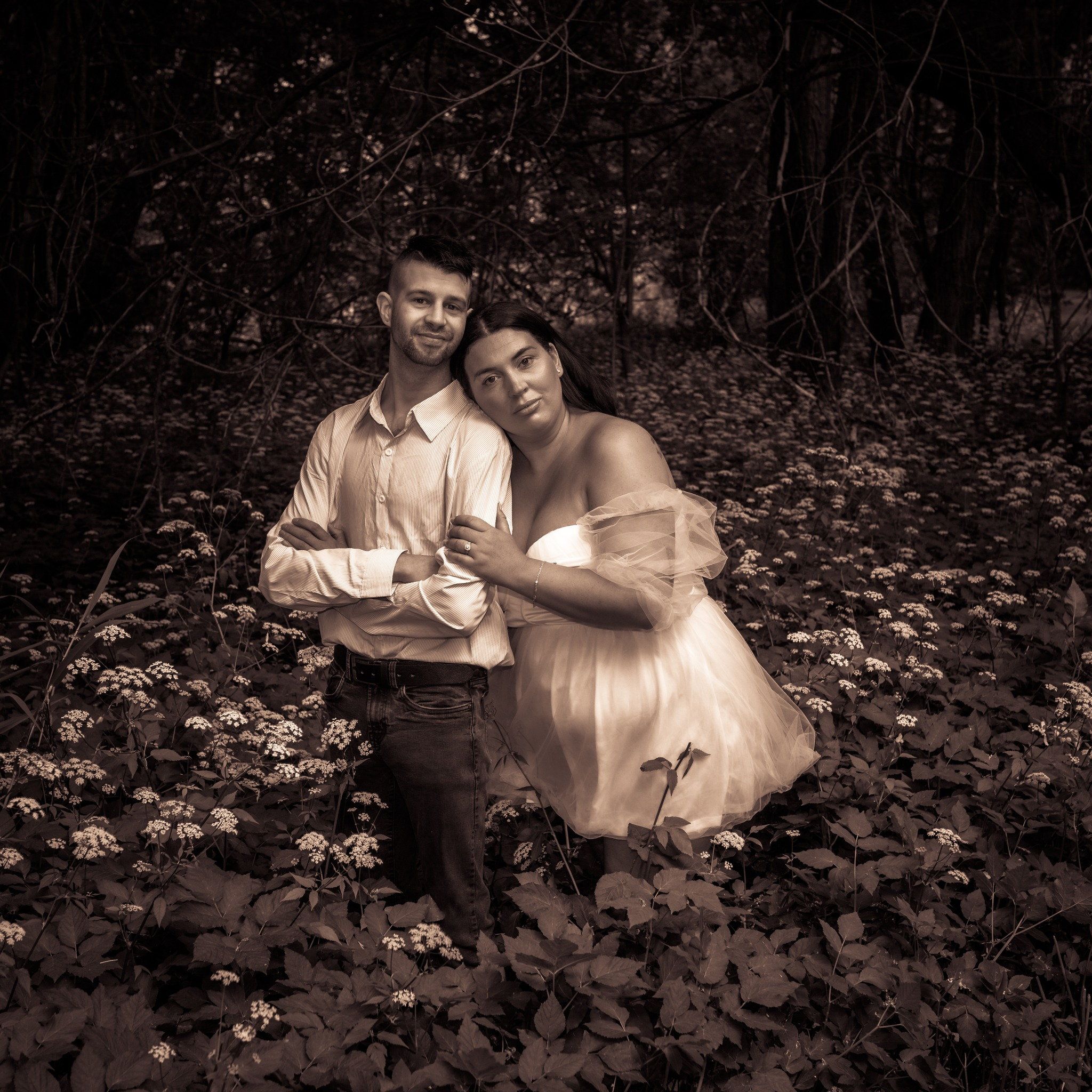 Warm-toned photo of a couple kneeling together in deep fallen leaves