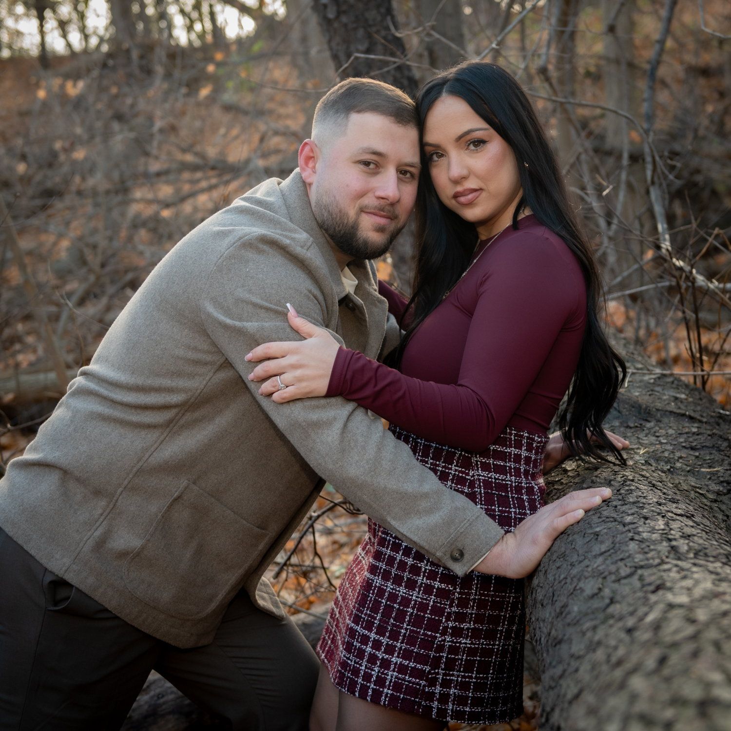 A couple leaning against a stone wall, her in a burgundy top and plaid skirt