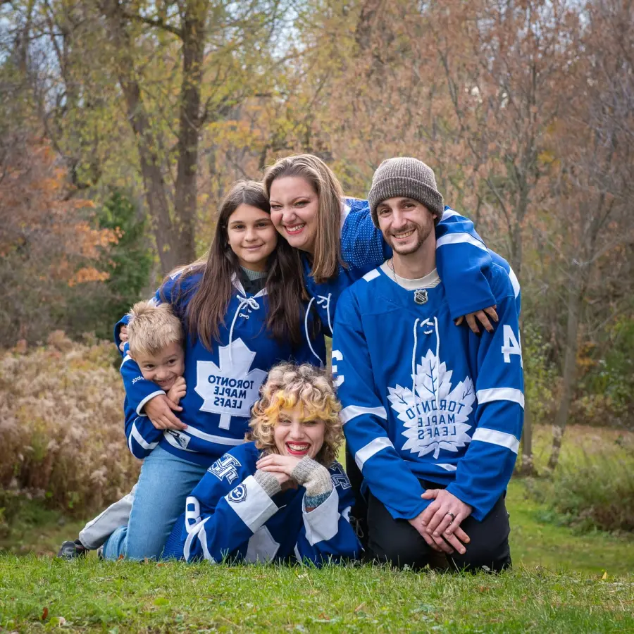 A family of five in Toronto Maple Leafs jerseys crouched together on autumn grass