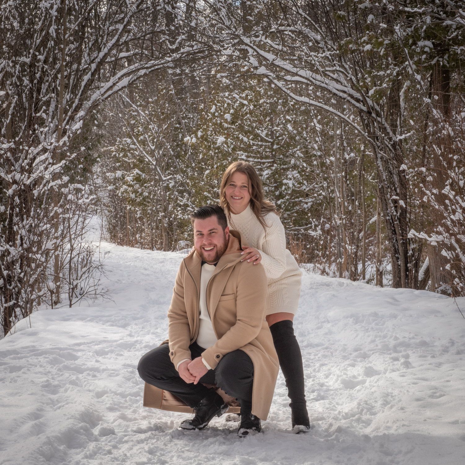 Carmela & James crouching together in fresh snow under a white-dusted canopy