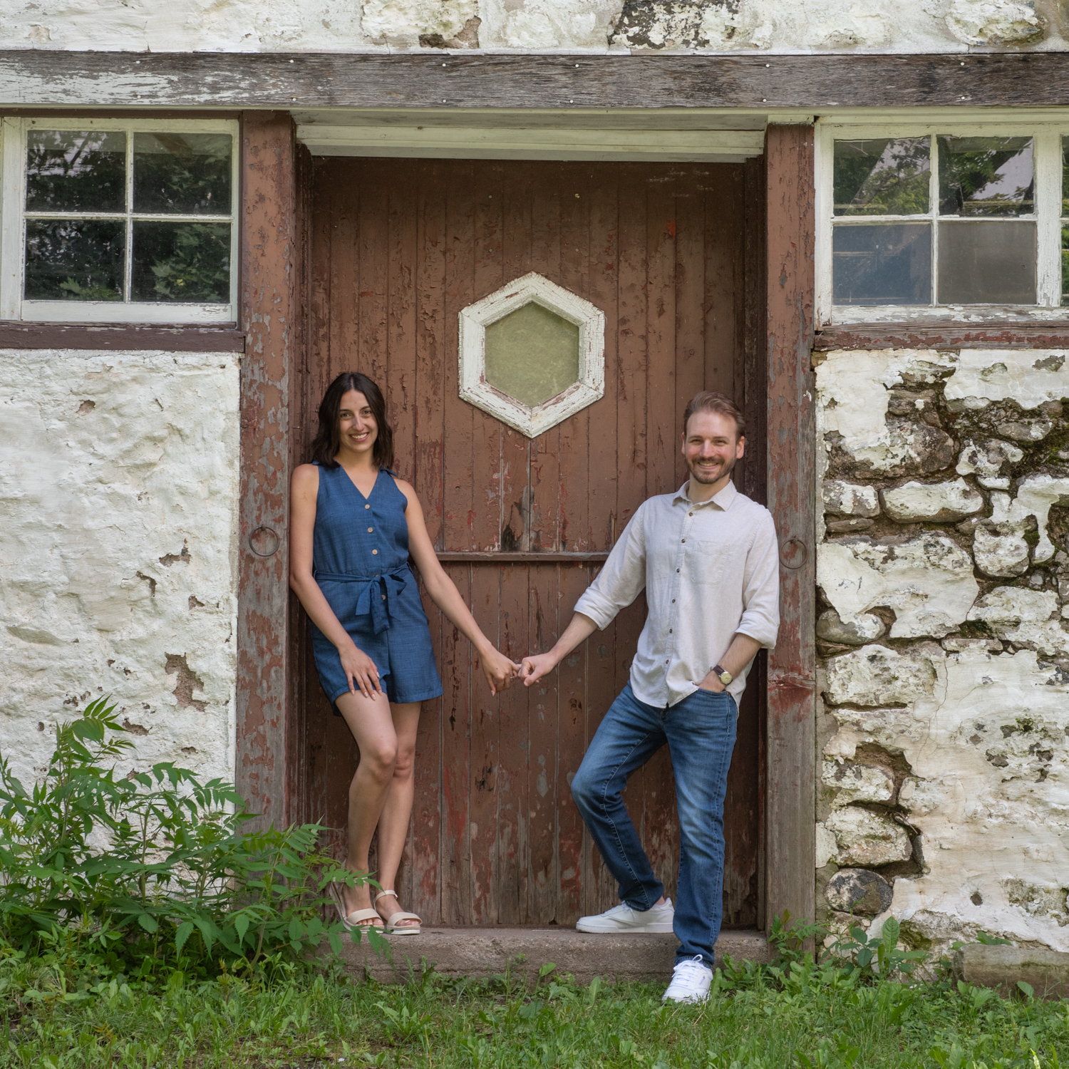 A couple holding hands in front of an old wooden door in a fieldstone wall