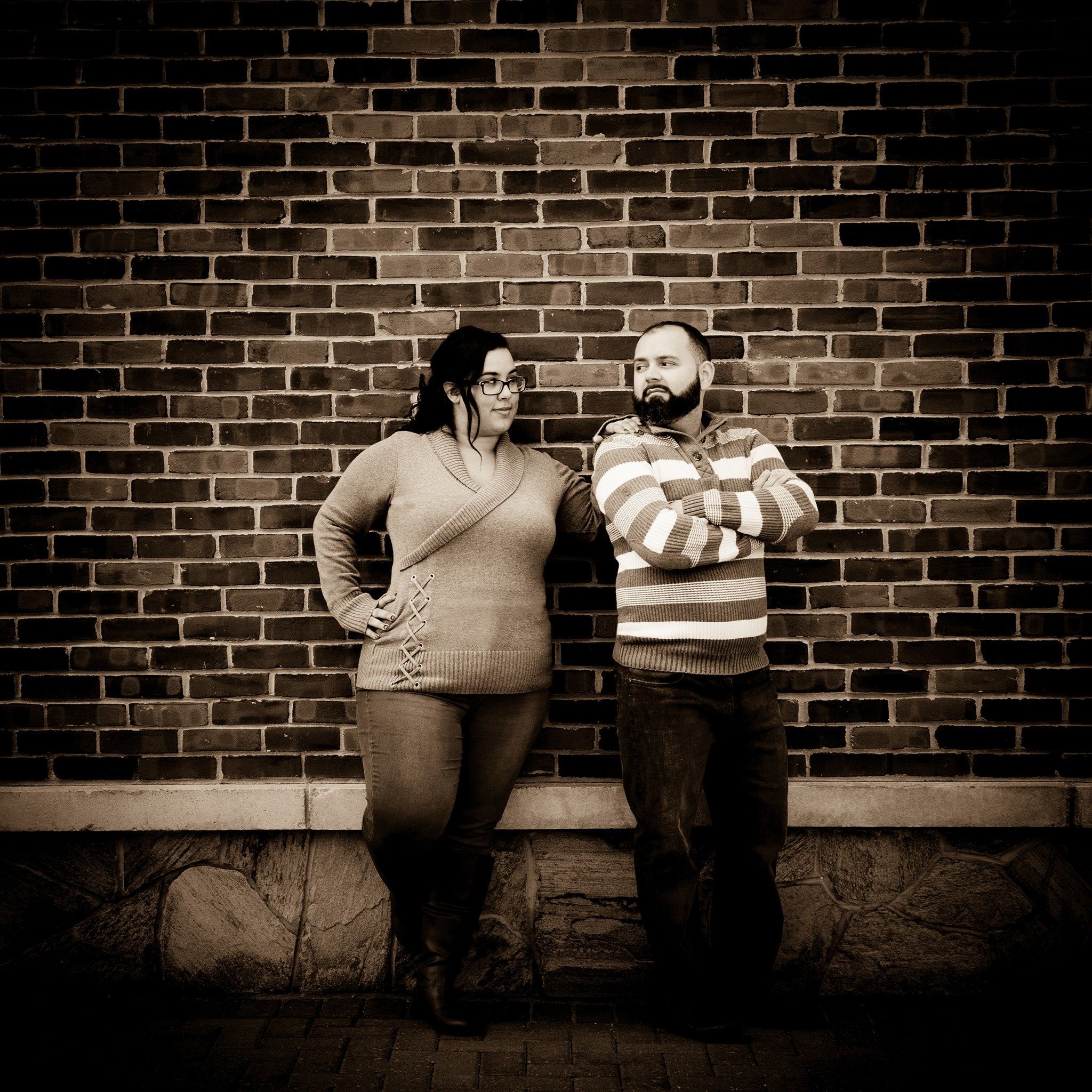 Dramatically lit photo of a couple standing against an old brick wall