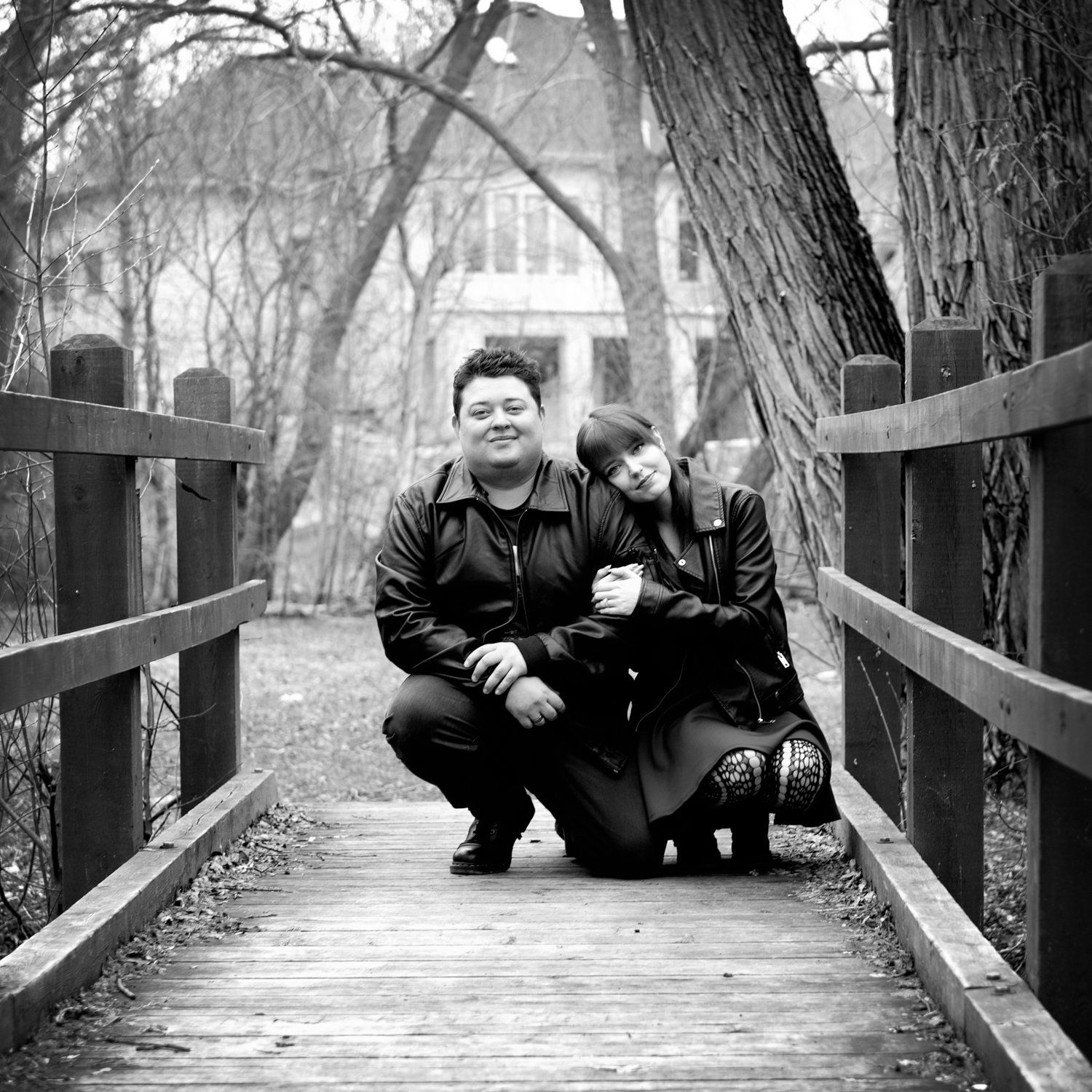 Black-and-white photo of a couple crouching together on a wooden footbridge