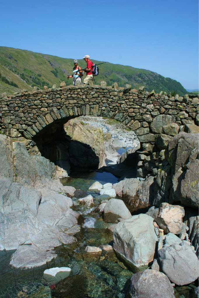 A stone packhorse bridge over a rocky beck below the fells
