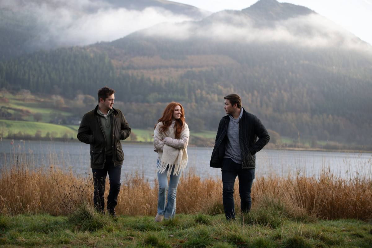 three people on the grassy shore of bassenthwaite lake with moody misty moutains in the background 