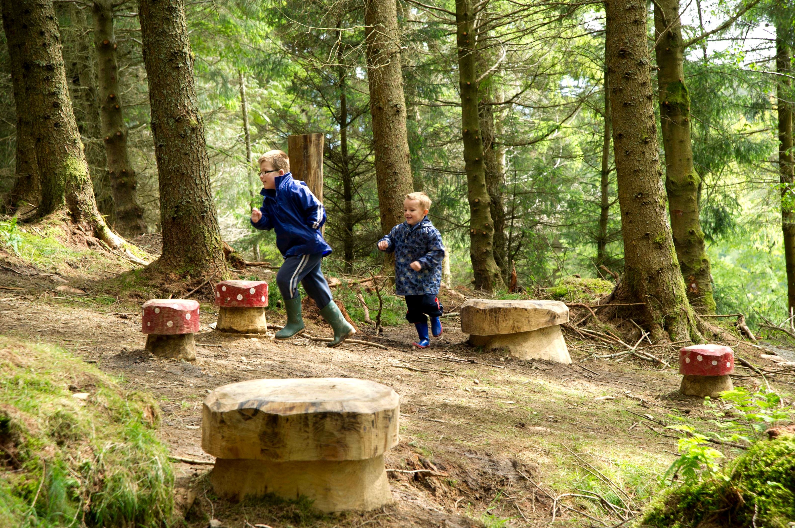 Two children playing among carved stone stools in a forest clearing