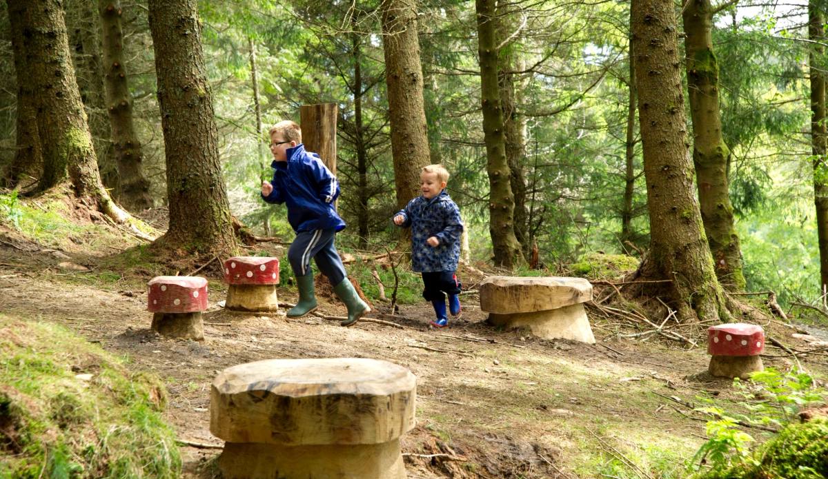 Two children playing among carved stone stools in a forest clearing