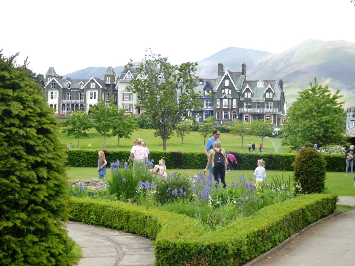 People on the lawns and flower borders of a large gabled hotel with the fells behind