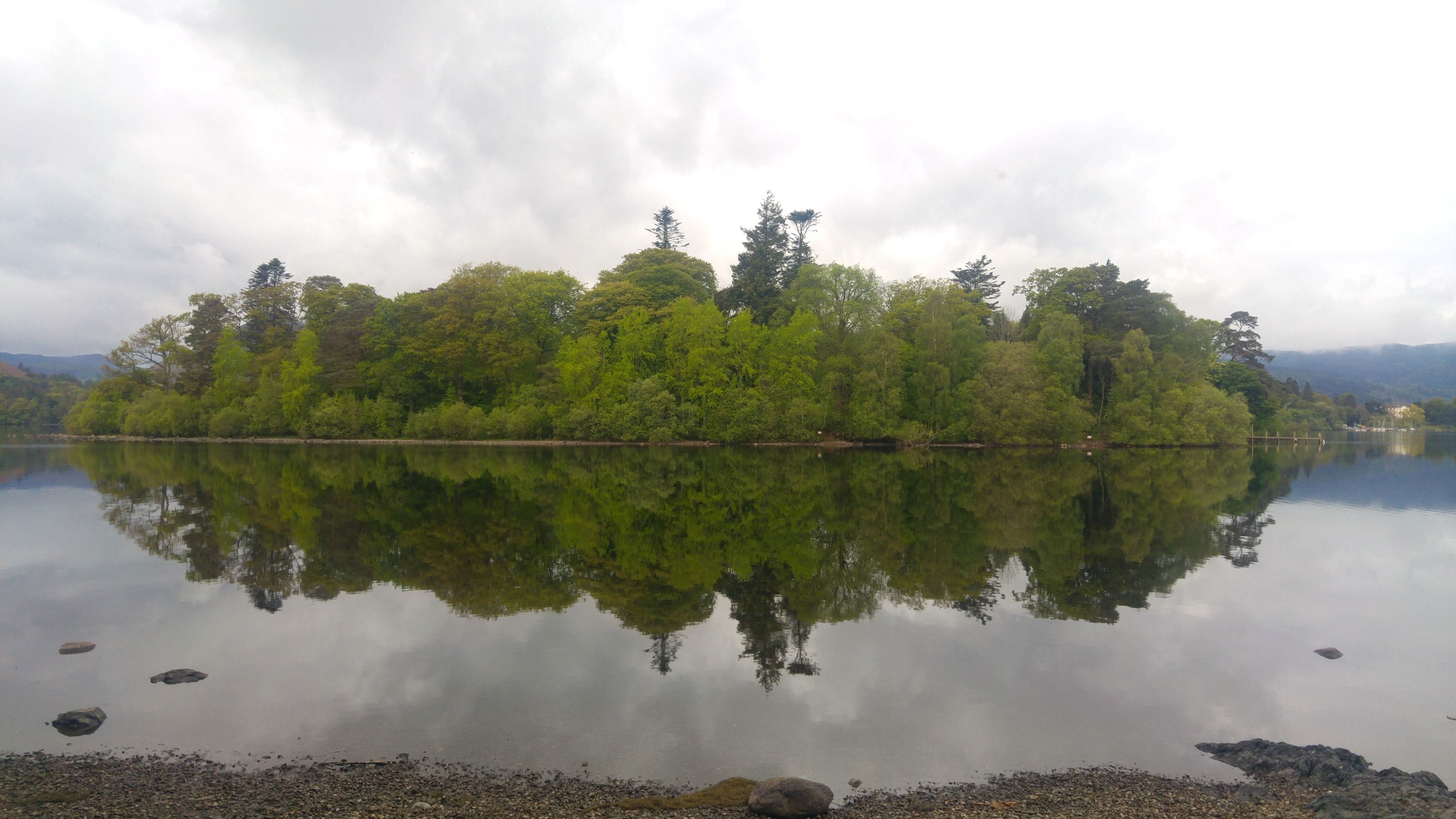 A densely wooded island mirrored in flat calm lake water
