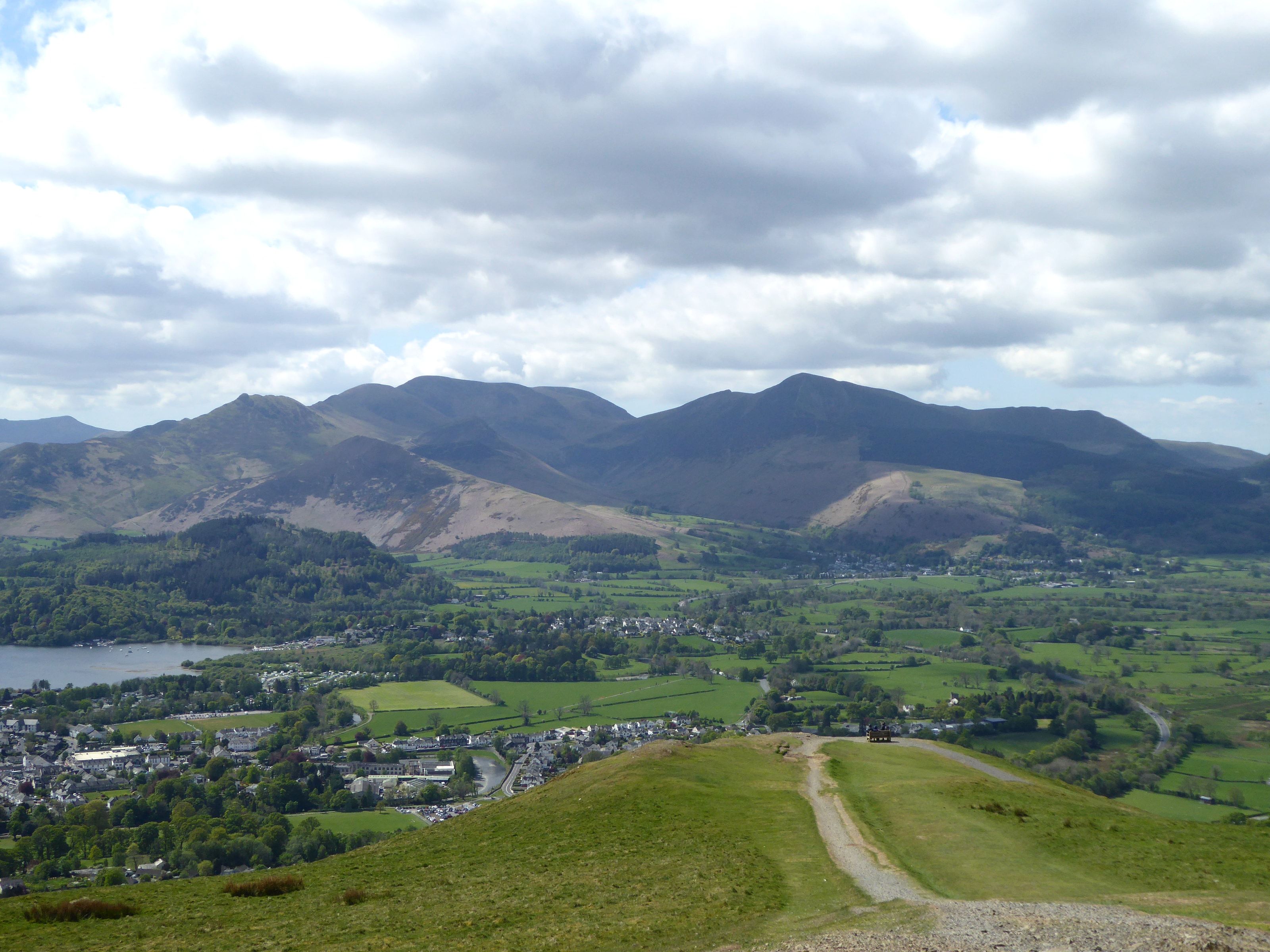 A wide grassy path curving off Latrigg with Keswick and the whole vale below