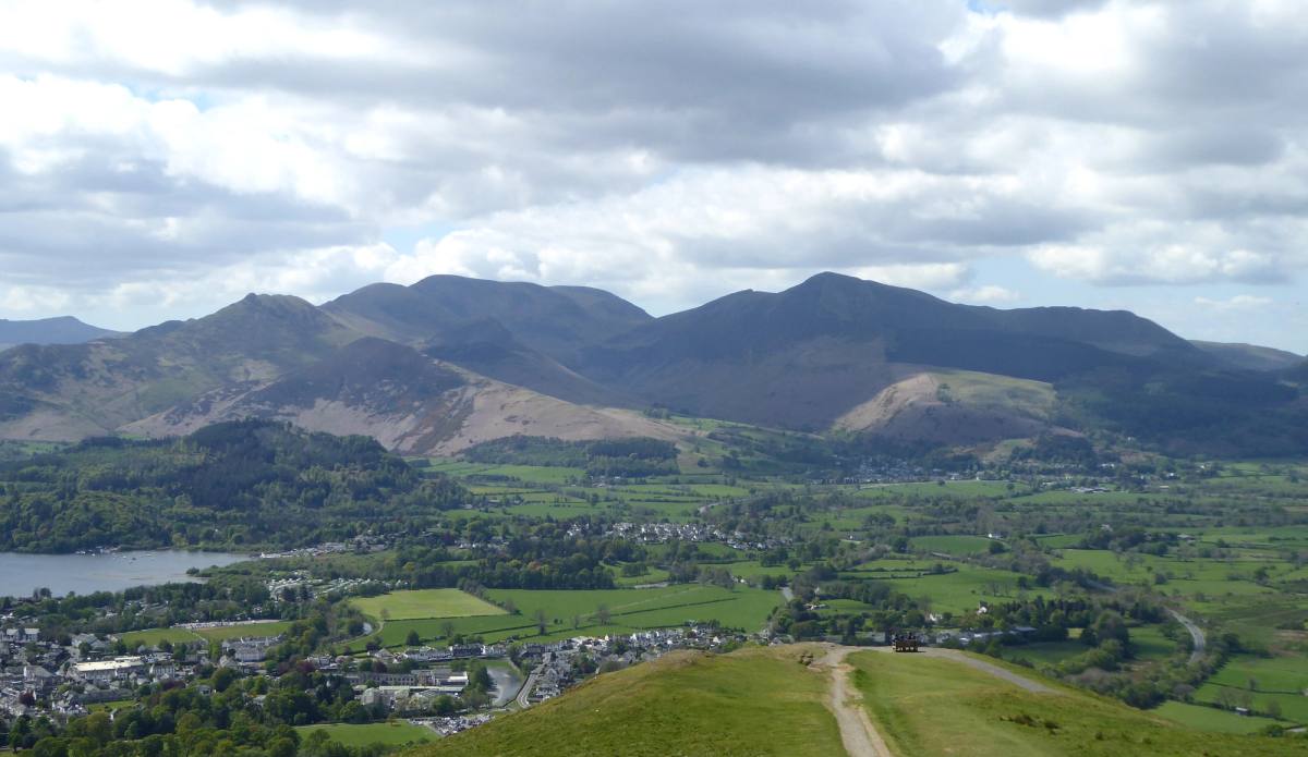 A wide grassy path curving off Latrigg with Keswick and the whole vale below