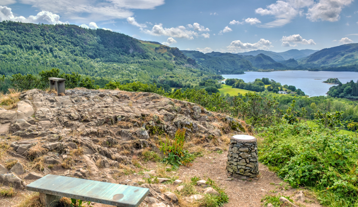 View from castlehead summit with a bench and a trig point waymarker with views across derwentwater
