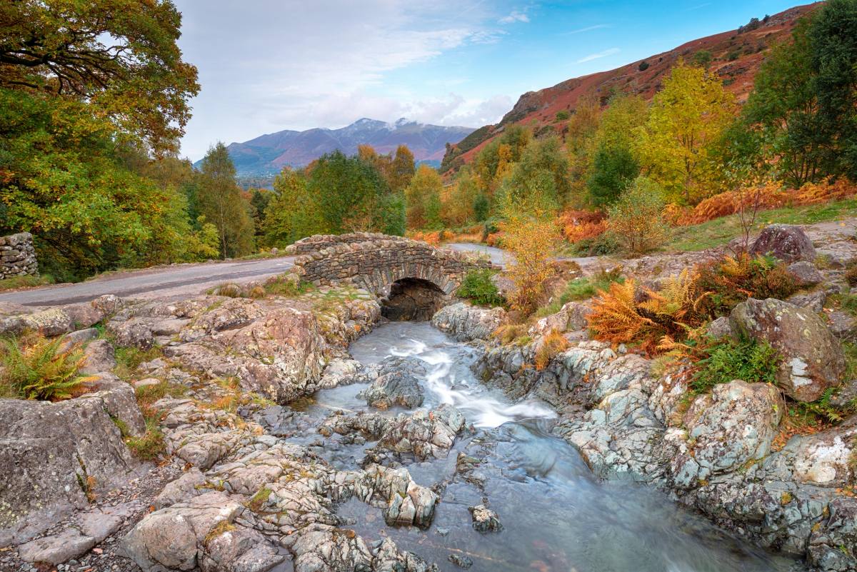 A stone packhorse bridge arching over the beck at Watendlath below the fells