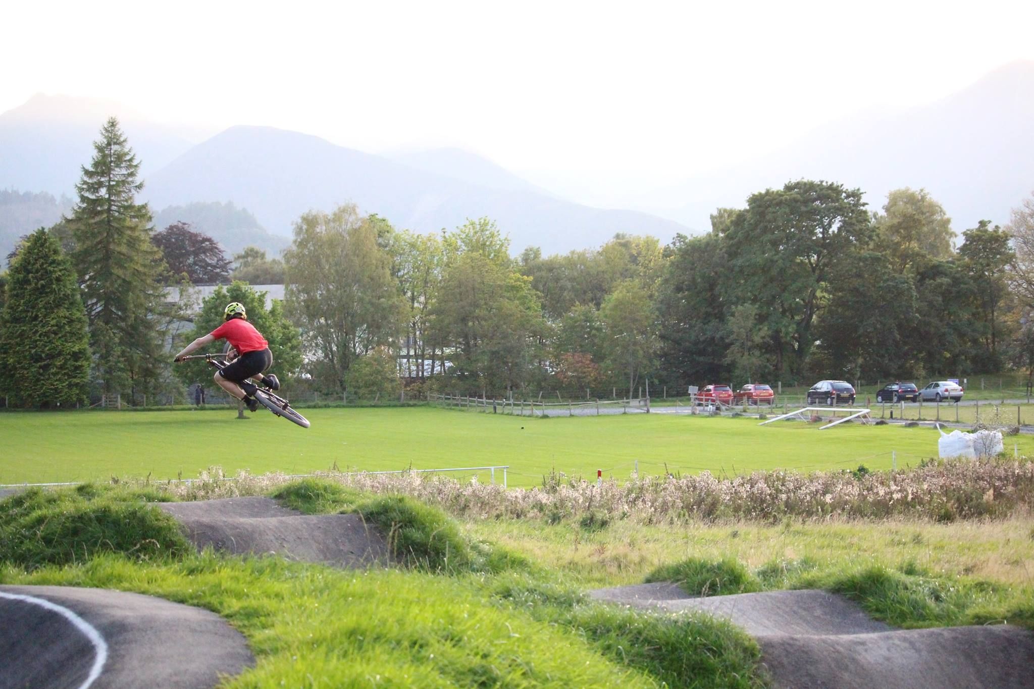 person and bike in the air doing a trick around a BMX tracking with lake and mountains in the distance