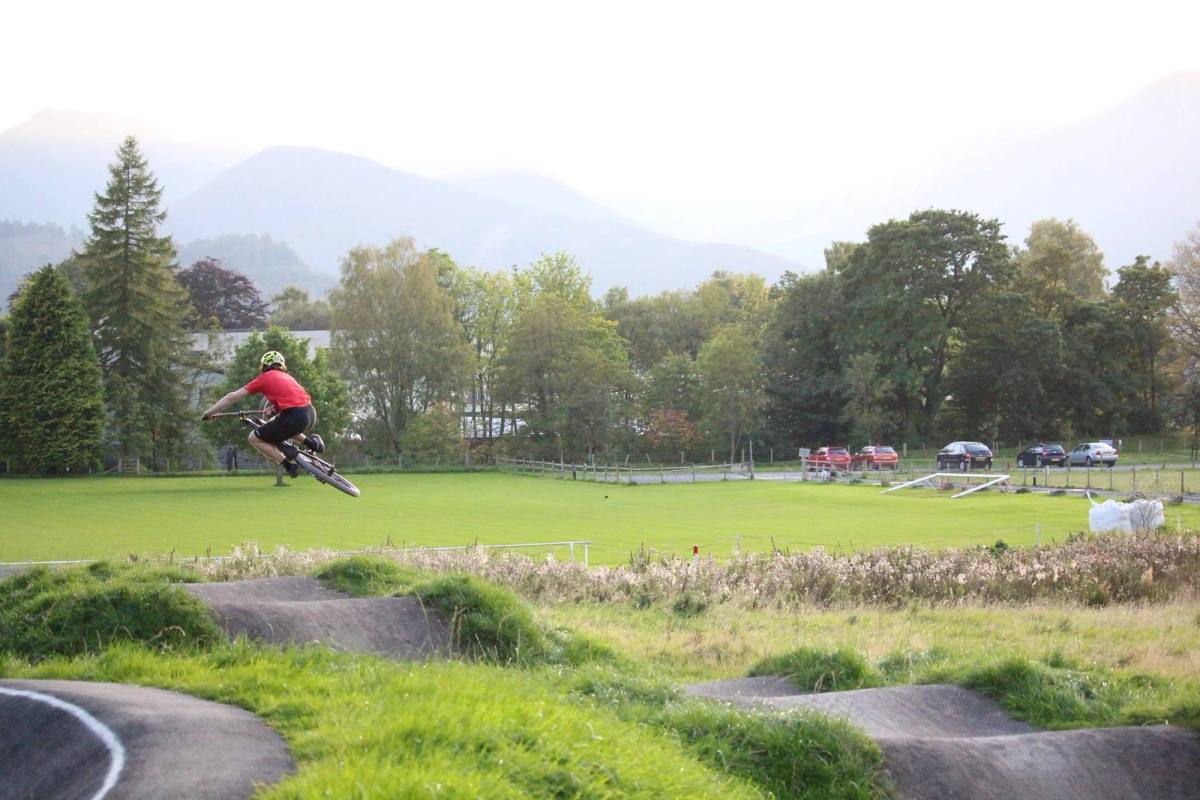 person and bike in the air doing a trick around a BMX tracking with lake and mountains in the distance