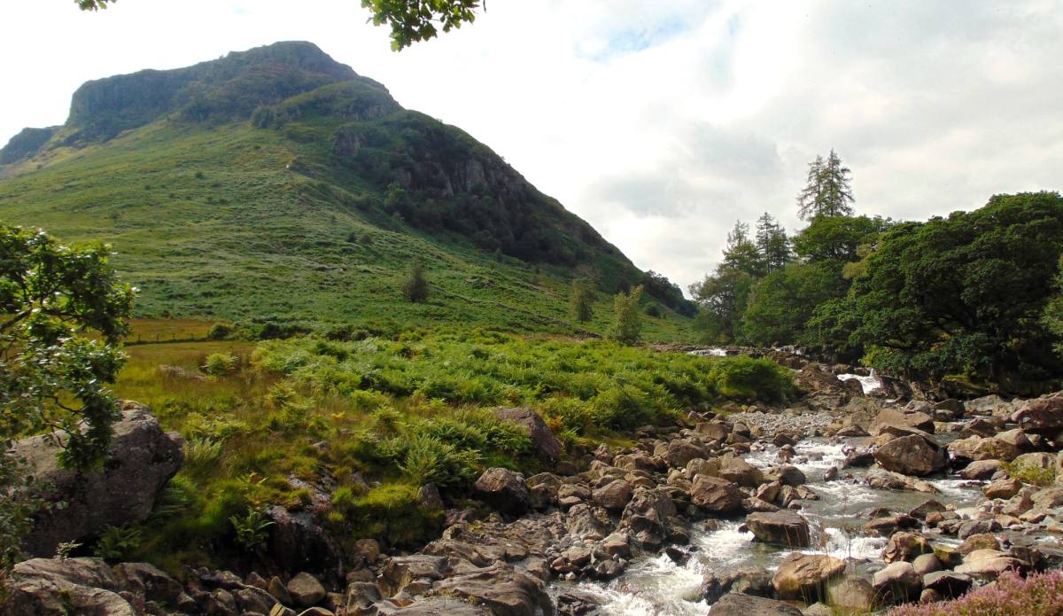 A beck running clear over rocks down the wide floor of the Langstrath valley