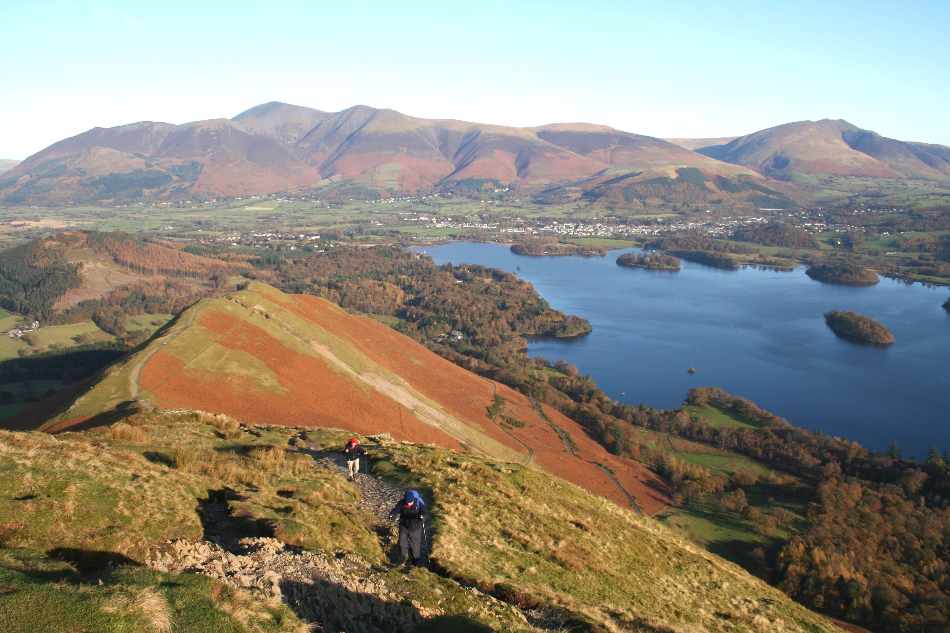 A walker on the red bracken ridge of Catbells with Derwentwater spread out below