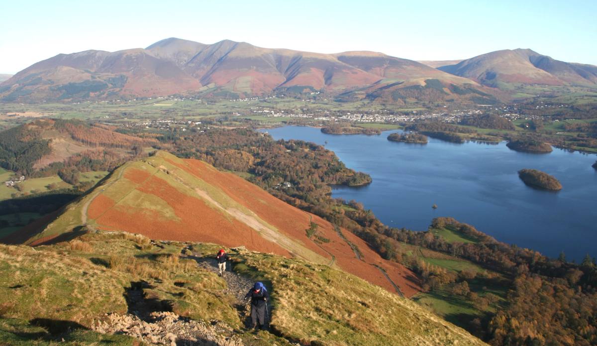 A walker on the red bracken ridge of Catbells with Derwentwater spread out below