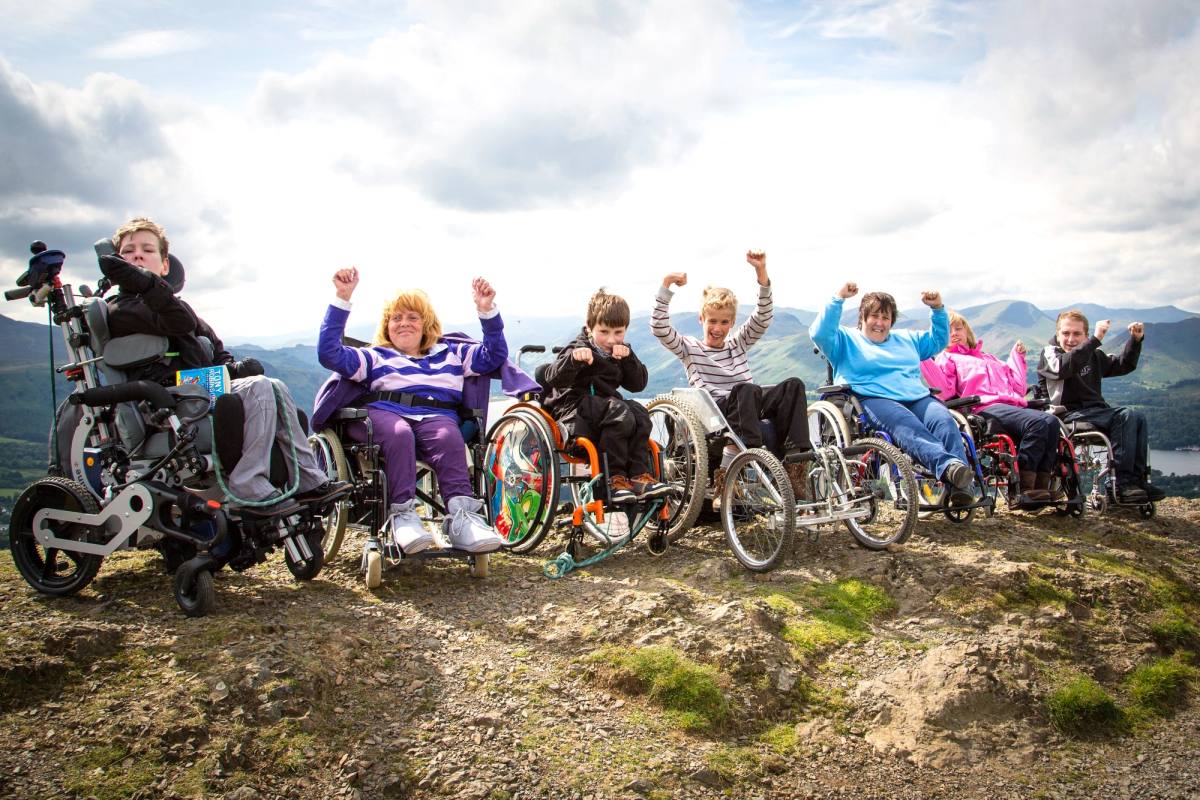 A group of adaptive cyclists and wheelchair users together with arms raised in celebration