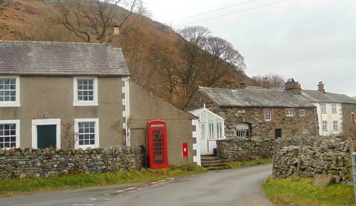A red telephone box against a rendered cottage on a quiet village road