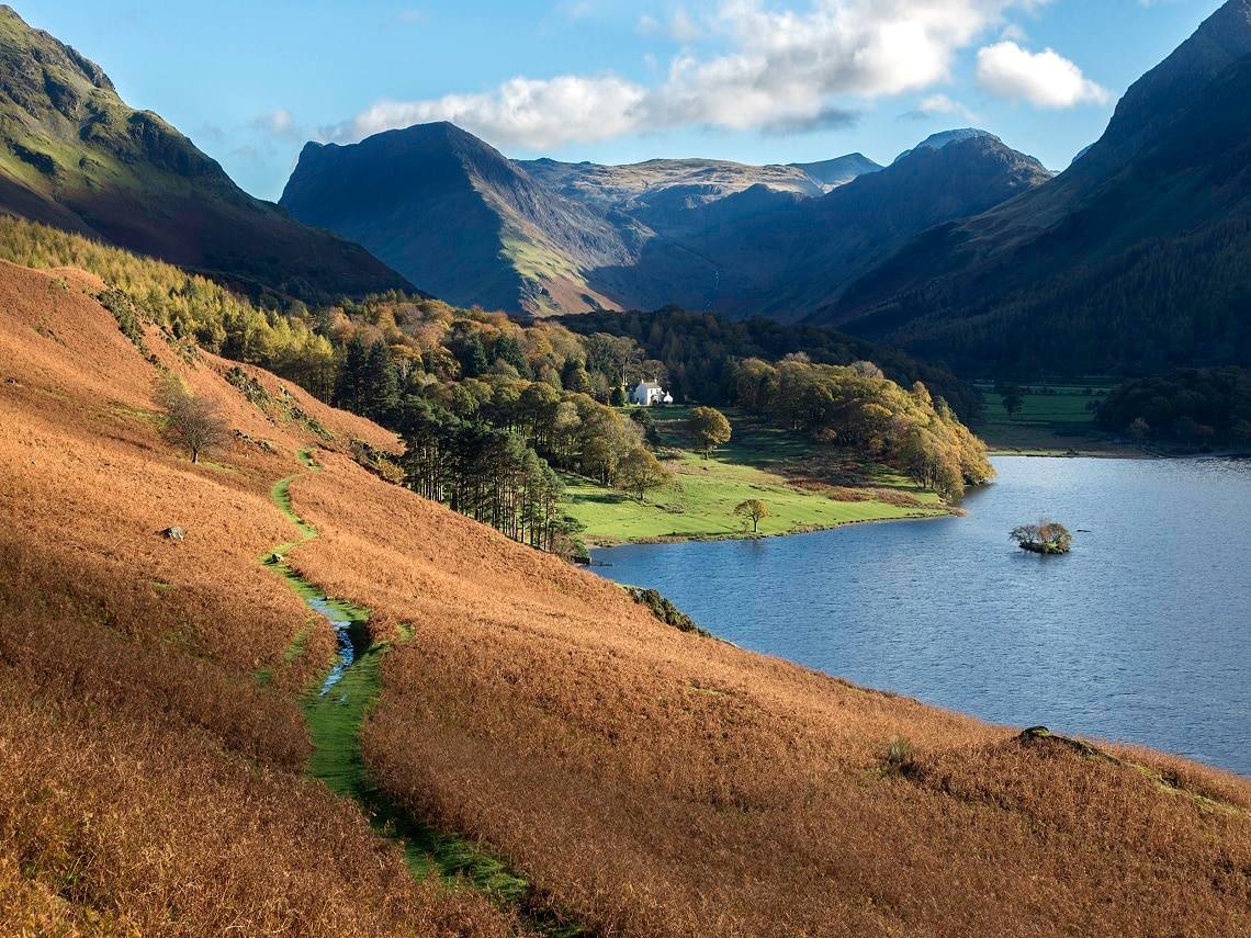 A walker on the bracken path along the shore of Buttermere below steep fells