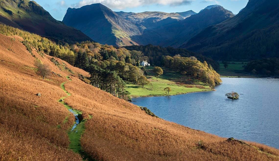 A walker on the bracken path along the shore of Buttermere below steep fells