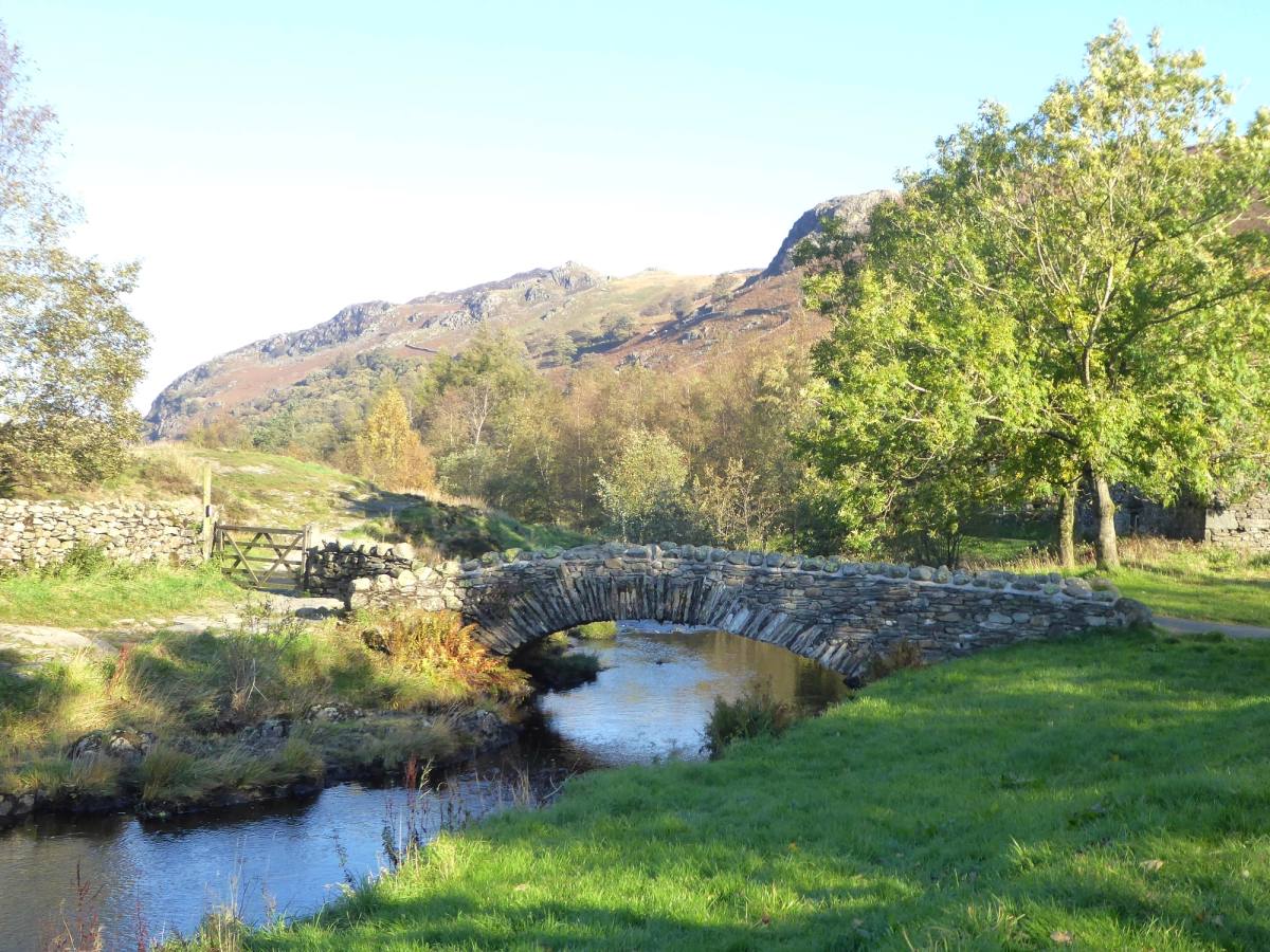 A stone packhorse bridge arching over the beck at Watendlath below the fells