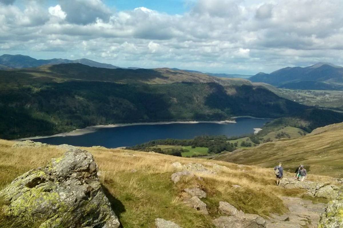 Thirlmere seen between rocky outcrops with walkers on the path below
