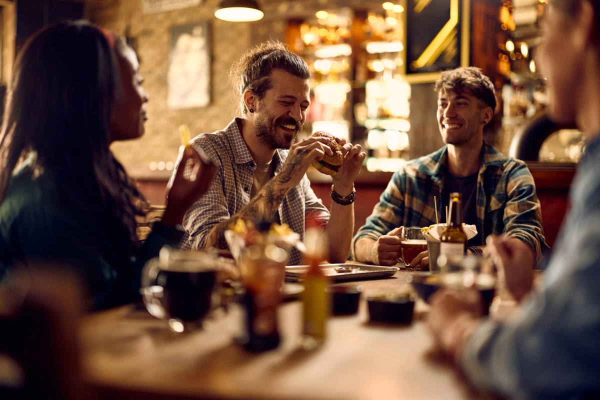 Friends around a pub table with burgers and drinks, laughing together