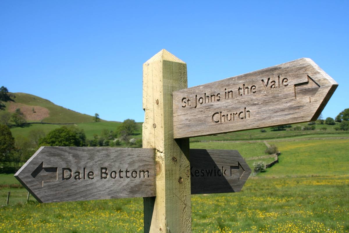 A weathered wooden fingerpost pointing to St Johns in the Vale Church and Dale Bottom