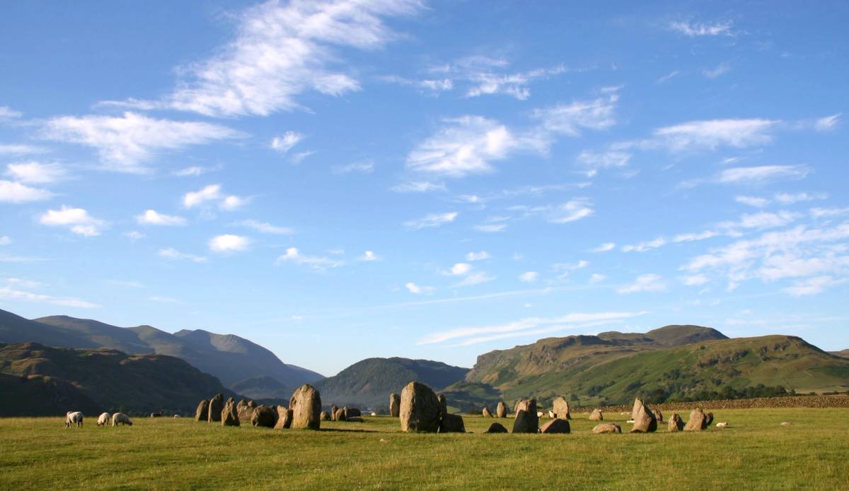 The Castlerigg stone circle on open grass under a wide sky of scattered cloud