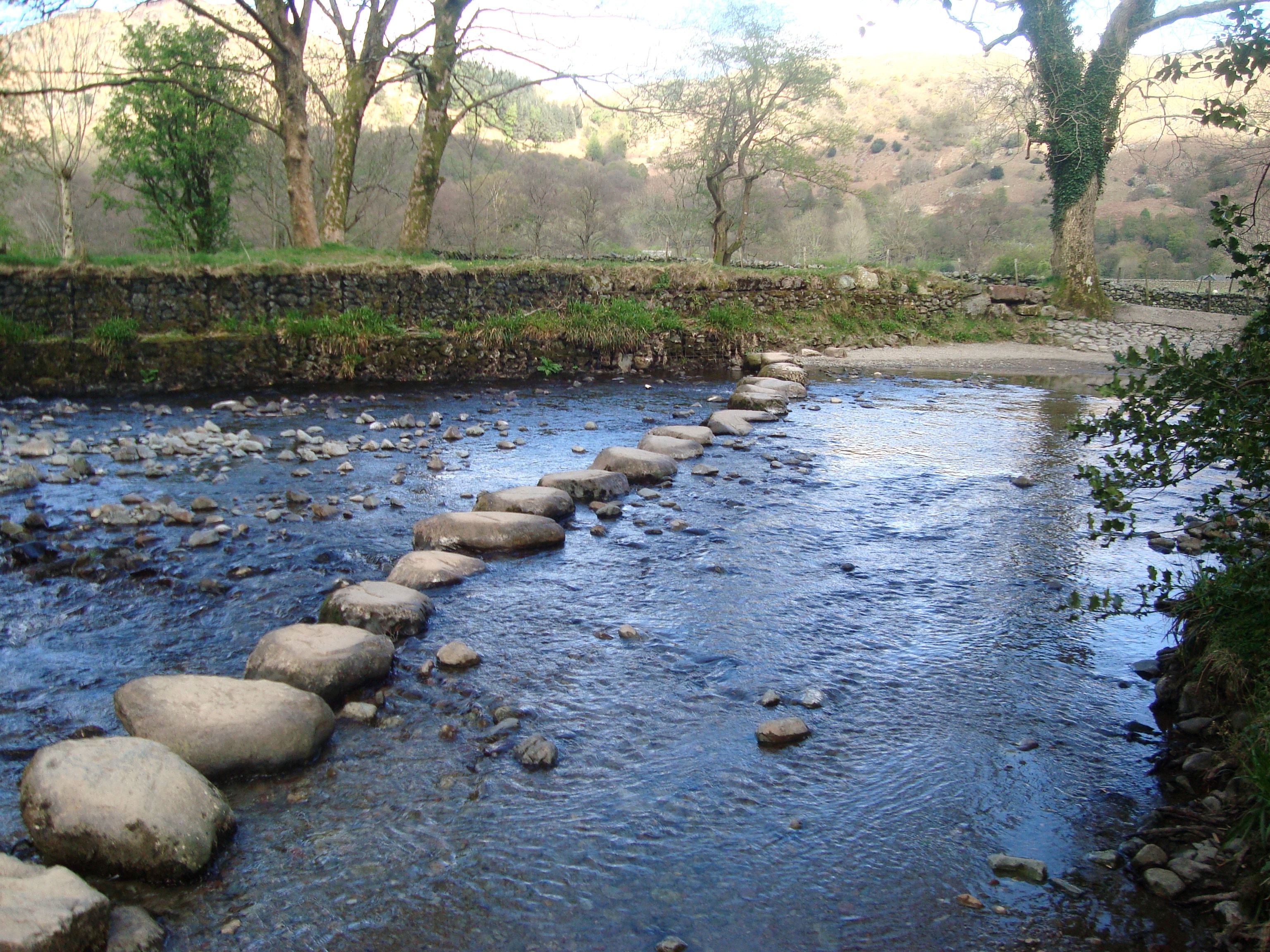 Large stepping stones crossing a shallow river between wooded banks