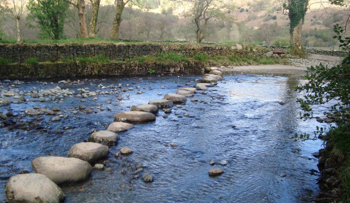 Large stepping stones crossing a shallow river between wooded banks