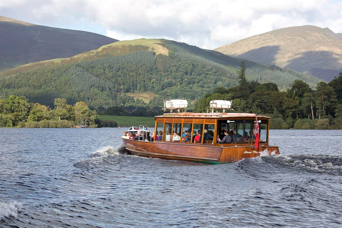 A crowded wooden launch running across Derwentwater with the fells behind