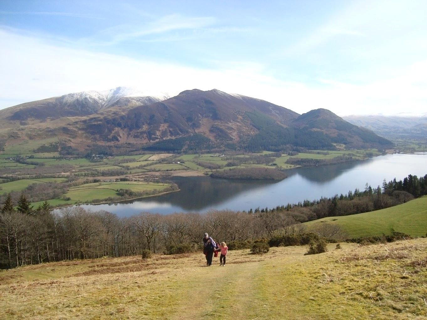 Two walkers on a forest track with Bassenthwaite Lake and Skiddaw spread out below