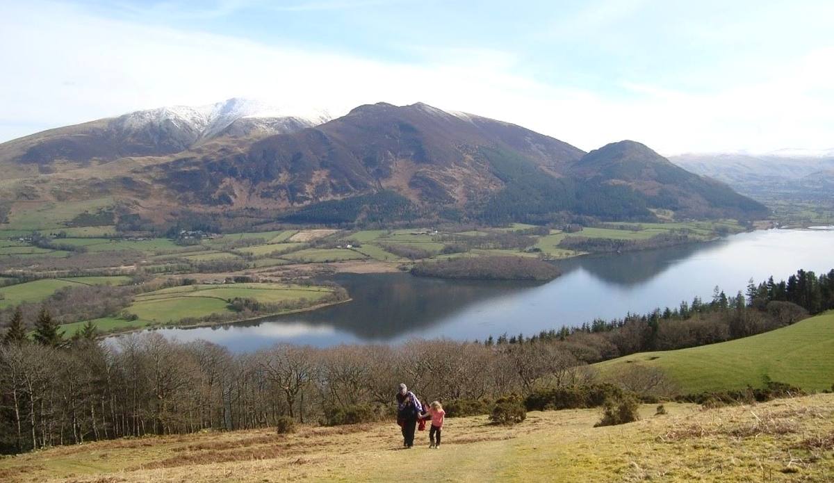 Two walkers on a forest track with Bassenthwaite Lake and Skiddaw spread out below