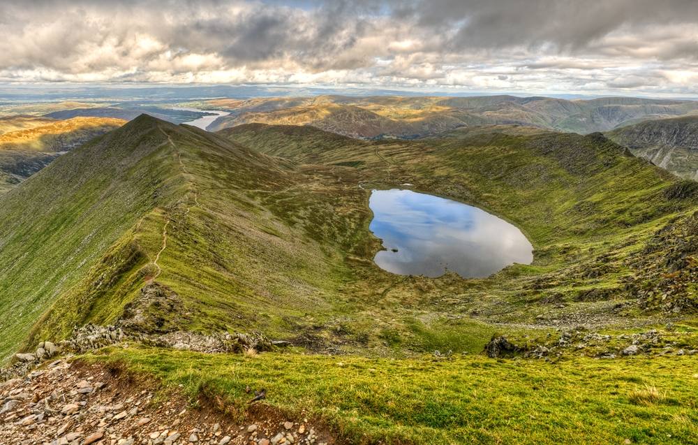birds eye view of red tarn small body of water nestled between two mountain ridges with a mountains and a lake in the background