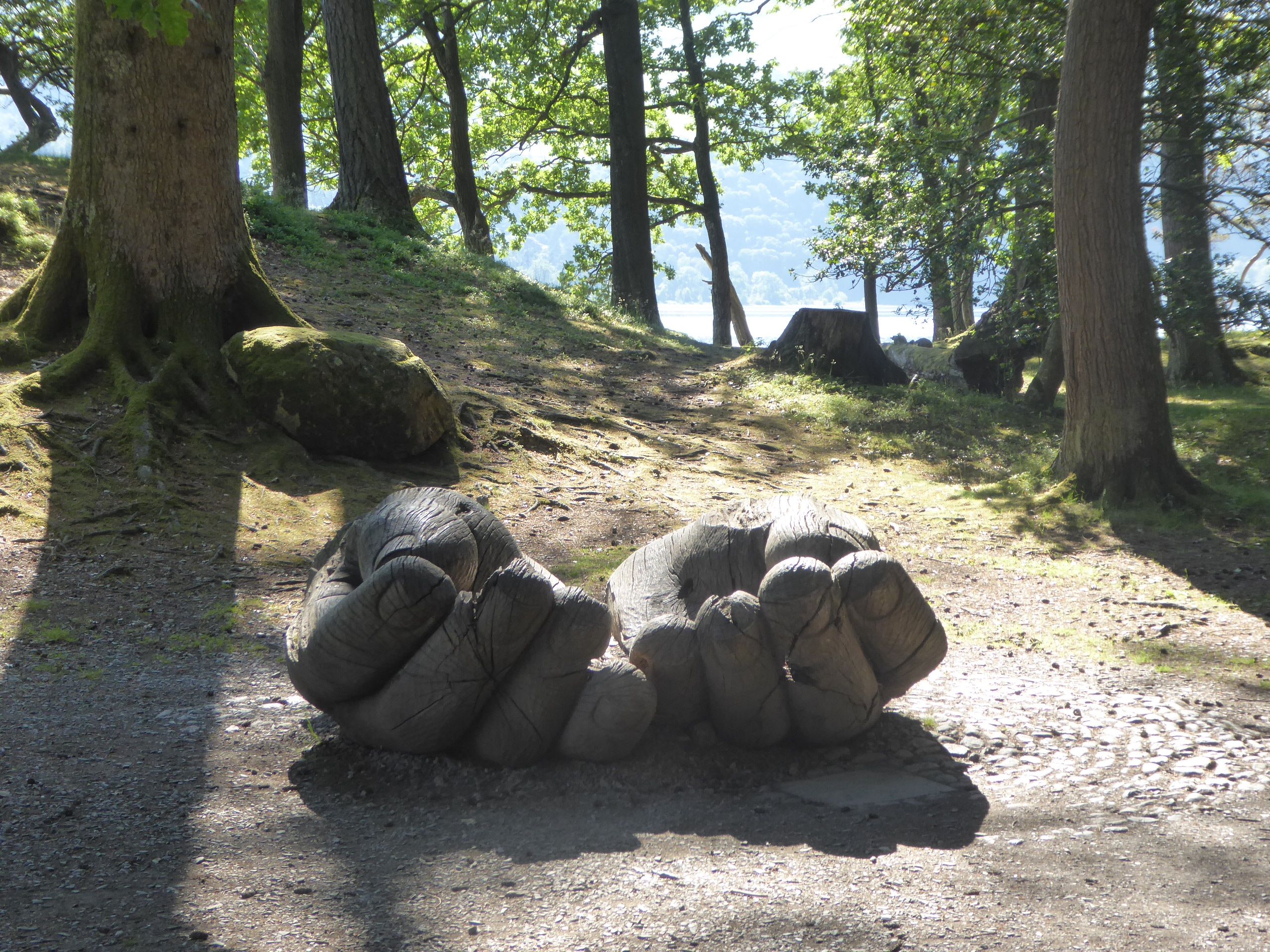 carved large hands sculpture in a woodland clearing with derwentwater lake in the background 