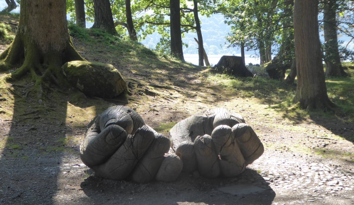 carved large hands sculpture in a woodland clearing with derwentwater lake in the background