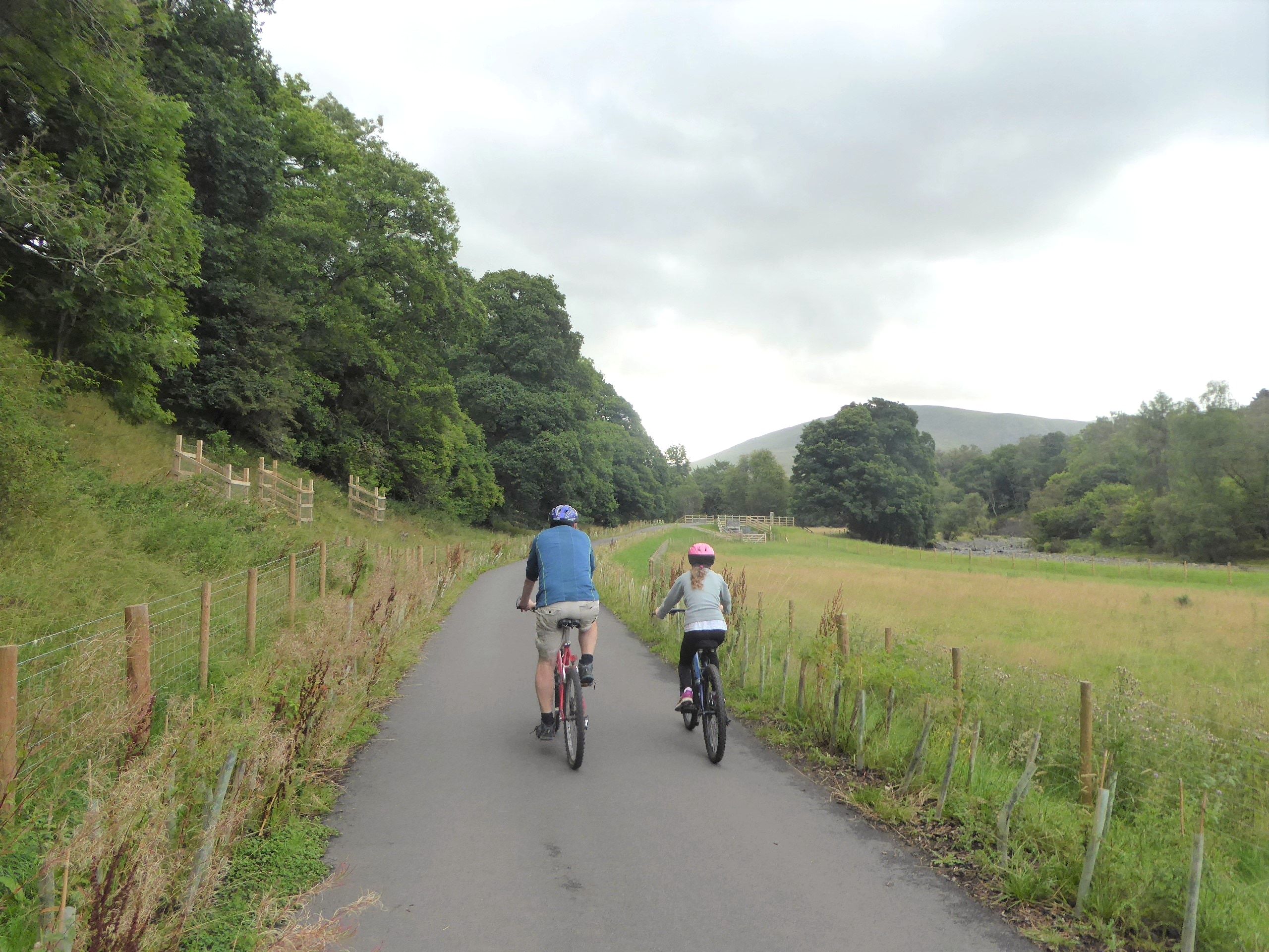Two cyclists riding side by side along the smooth railway path between fields