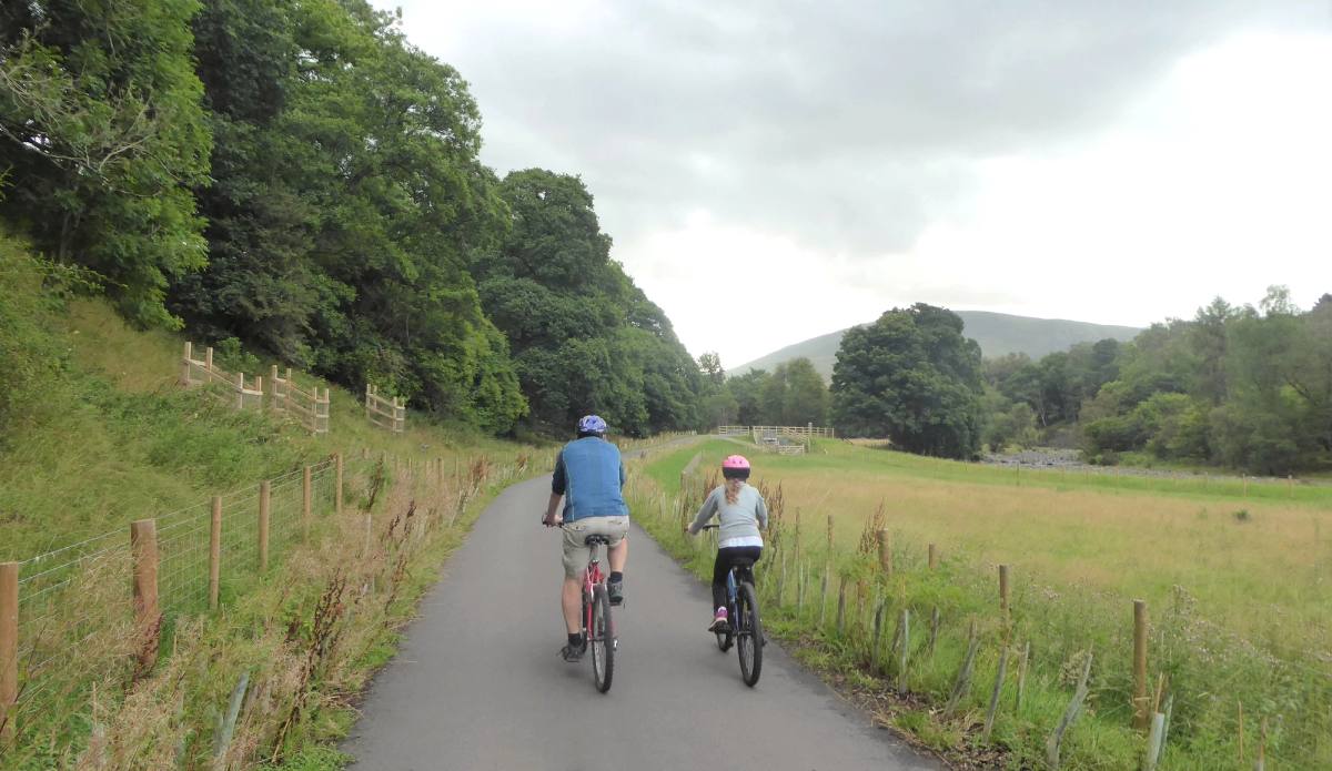 Two cyclists riding side by side along the smooth railway path between fields